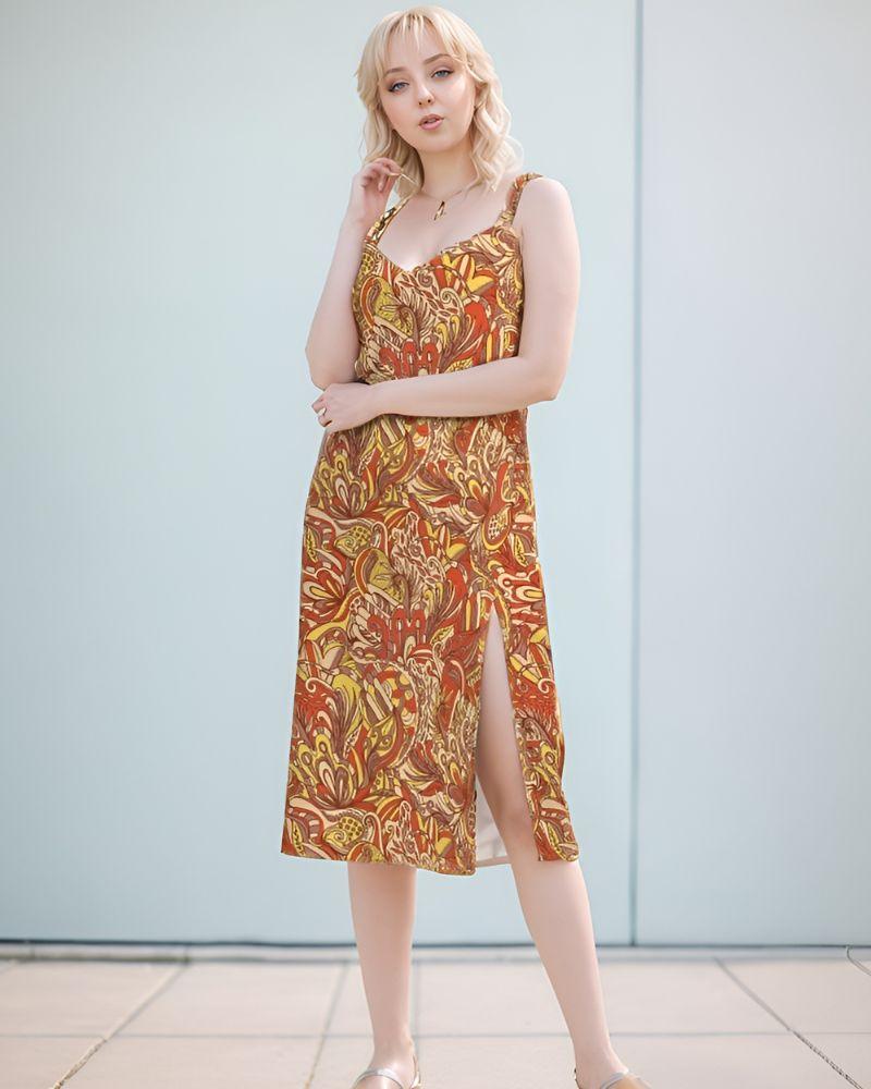 midi dress with a vibrant, psychedelic retro floral  print featuring swirling patterns in shades of red, yellow, and brown. The dress has a V-neckline, spaghetti straps, and a leg-baring side slit. Blissfully Brand