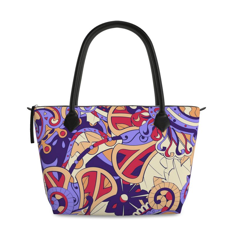 A vibrant Sechie Zip Top Tote Bag featuring a baroque paisley print with bright colors and intricate patterns against a cream background. The bag has black leather handles and a zip top closure. It is a stylish and practical everyday bag. Blissfully Brand