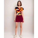 Trendy cropped women's t-shirt with bold abstract geometric pattern in orange, burgundy, navy, and white. Short-sleeved summer top with vibrant retro-inspired print, paired with burgundy mini skirt for a stylish casual outfit.