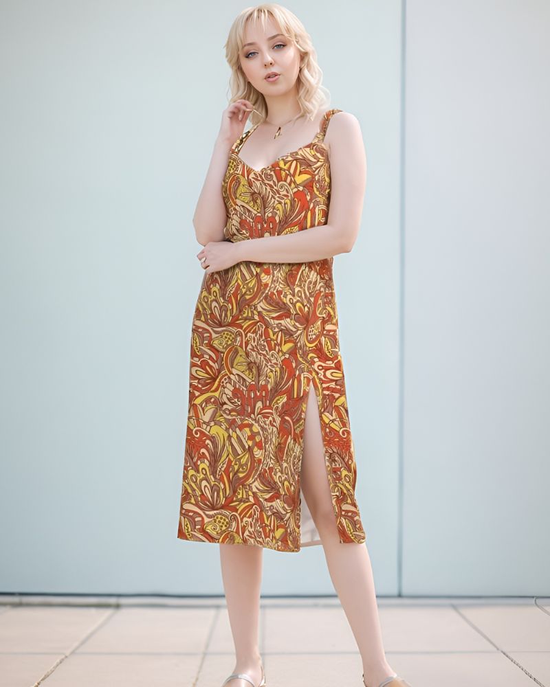  midi dress with a vibrant, psychedelic retro floral  print featuring swirling patterns in shades of red, yellow, and brown. The dress has a V-neckline, spaghetti straps, and a leg-baring side slit. Blissfully Brand