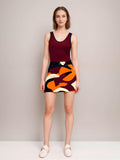 Stylish women's outfit: burgundy tank top paired with vibrant abstract print mini skirt in orange, maroon, and cream